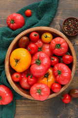 Bowl with different fresh tomatoes on wooden background