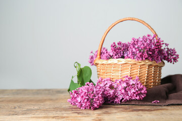 Fototapeta na wymiar Wicker basket of beautiful lilac flowers on wooden table near white wall