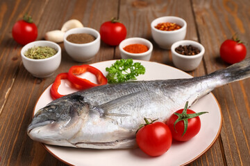 Plate of raw dorado fish with tomatoes on wooden background