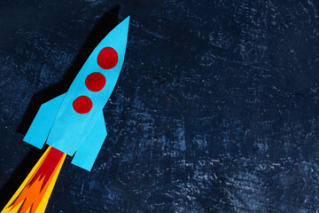 Blue paper rocket on dark grunge background