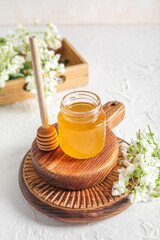 Jar of honey with flowers of acacia and dipper on light background, closeup
