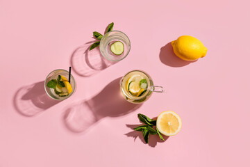 Glasses and jug of lemonade with cucumber on pink background