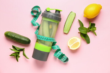 Sports bottle of lemonade with cucumber and measuring tape on pink background