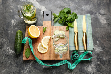 Mason jars of lemonade with cucumber and measuring tape on grey background