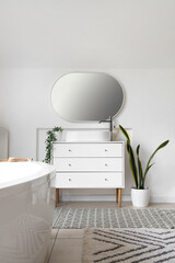 Interior of light bathroom with bathtub and sink on chest of drawers