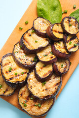 Board with delicious grilled eggplants on light blue background