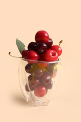 Glass with sweet cherries and leaf on orange background