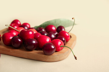 Board with sweet cherries on beige background