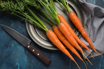 Plate of fresh carrots with leaves on blue background