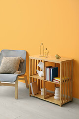 Shelving unit with books, decor and chair near orange wall in room