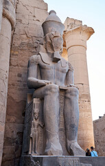 Seated statue of Ramesses II by the First pylon of the Luxor Temple, Egypt. Columns and statues of...
