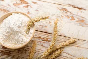 Bowl with wheat flour and spikelets on white wooden table, closeup
