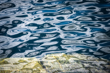 The striped edge of a rock is visible through the waves, which reflect the sky in every ripple. Like a painting.