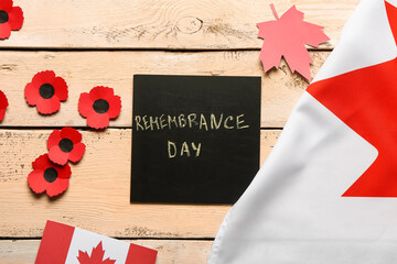 Poppy flowers with flags of Canada and card on beige wooden background. Remembrance Day