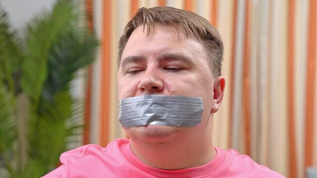 Portrait of man with his mouth taped shut, hostage, apartment robbery, asking for information, safe code, secret victim of domestic violence resists, willpower of oppositionist, unbending character