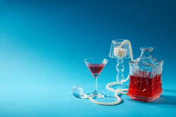 Front view of whiskey glass with decanter vertical decorated with glass ball and pearl necklace on a blue background. Blank space for design and add text