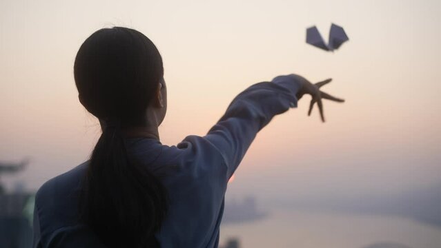 young female flying paper plane at sunset