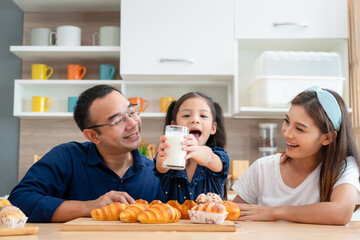 Father, mother, and daughter enjoying breakfast together in the kitchen, Kid girl drinking milk, Happy Asian family concepts