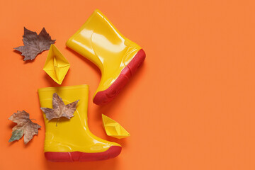 Yellow gumboots with autumn leaves and paper ships on orange background