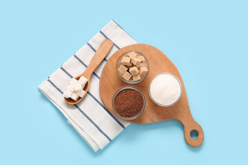 Bowls and spoon with different types of sugar on blue background