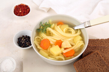 Bowl of tasty chicken soup and bread on white background