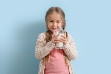 Cute little girl with glass of tasty milk on blue background