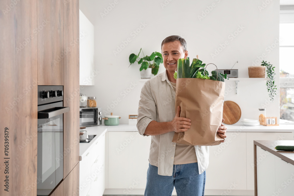 Wall mural Mature man with paper bag of fresh vegetables in kitchen