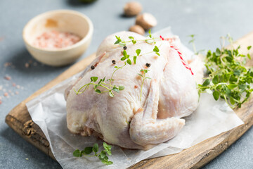 organic raw whole chicken with thyme peppers and garlic on a rustic table
