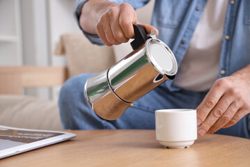 Mature man pouring espresso from geyser coffee maker into cup at home, closeup