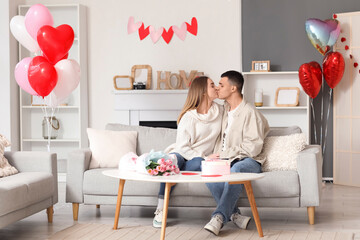 Beautiful young couple with gift box, bouquet of flowers and heart-shaped balloons celebrating...