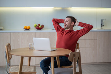 Positive carefree man freelancer, IT programmer, developer, sales manager, working with notebook at home, sitting, resting, straightening back after successful job ending, genius idea realization 