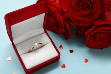 Box with beautiful engagement ring and red roses on blue background