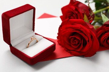 Box with beautiful engagement ring, envelope and red roses on white background