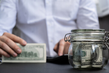 Dollar Banknote Saving Money In Glass Jar. Unrecognizable man calculate money on calculator...