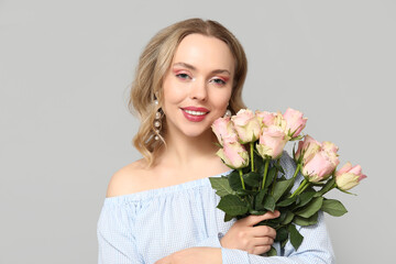 Happy young woman with bouquet of beautiful roses on grey background