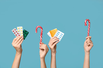 Female hands holding pills in blister packs and candy canes on blue background - obrazy, fototapety, plakaty