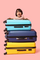 Beautiful young shocked woman with suitcases on pink background. Winter vacation concept