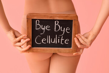 Beautiful young woman holding board with text BYE BYE CELLULITE on pink background, back view - obrazy, fototapety, plakaty