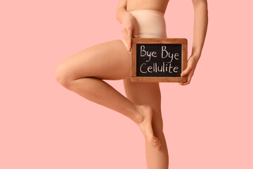 Beautiful young woman holding board with text BYE BYE CELLULITE on pink background - obrazy, fototapety, plakaty