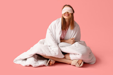 Beautiful young happy woman with soft blanket and sleeping mask sitting on pink background