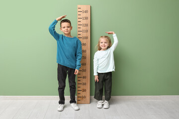 Cute little children measuring height near green wall