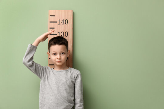 Cute little boy measuring height on green background