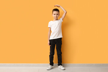 Fototapeta na wymiar Cute little boy measuring height near yellow wall