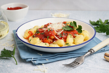 Plate of tasty gnocchi with tomato sauce and cheese on blue background