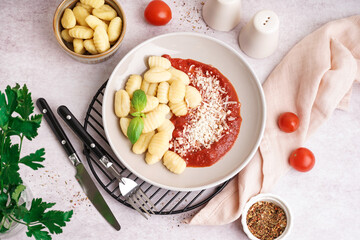 Plate and bowl of tasty gnocchi with tomato sauce and cheese on white background