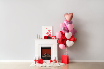 Fireplace with heart-shaped balloons and gift boxes near white wall. Valentine's Day celebration