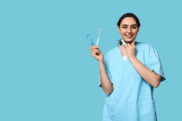 Young female dentist with toothbrush and tongue scraper on blue background - obrazy, fototapety, plakaty