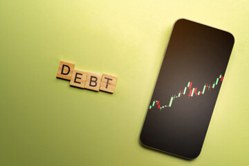 Stock chart on the mobile phone screen and a wooden cube with a Debt letter