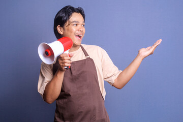 Happy Asian guy wear apron talk loudly using megaphones making announcement and presenting empty space for text or ads