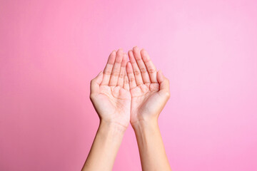 Hands showing praying hands gesture isolated on pink background.